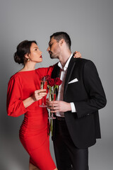 Side view of sexy woman in dress hugging boyfriend with champagne and roses on grey background.