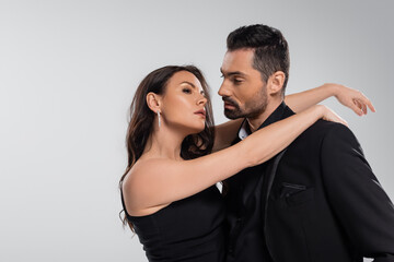 dreamy woman hugging bearded man in black suit isolated on grey.