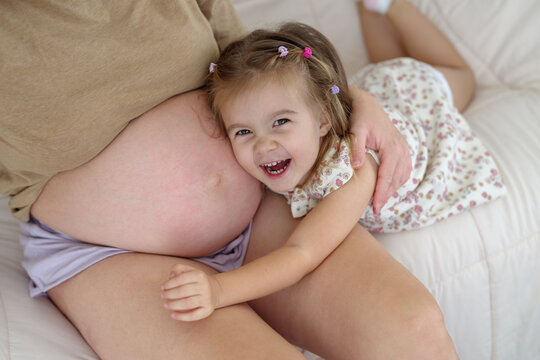 Close-up of a beautiful girl hugging mother’s pregnant belly with a smile