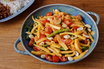 Papaya salad with green beans, lime wedges, tomatoes and peanuts. Fresh Thai style exotic salad from ripe papaya fruit.