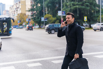 Middle-aged Caucasian businessman talking on the phone crossing the road on his way to work