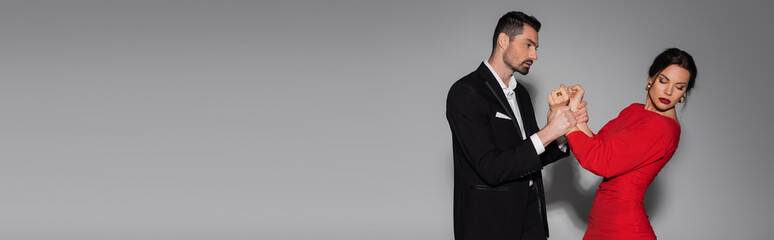 Bearded man in suit holding hands of elegant girlfriend on grey background, banner.