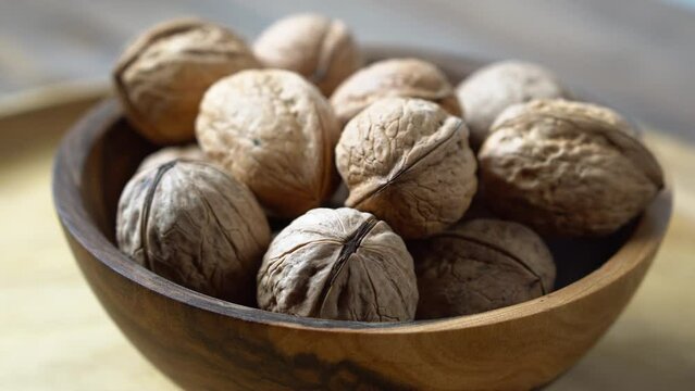 Rotating walnuts in a shell in a wooden bowl on a wooden background.