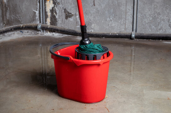 Bucket with mob in flooded basement or electrical room. Cleaning up lots of water on floor from multiple leaks in wall and ceiling. Water damage from rain, snowmelt or pipe burst. Selective focus.