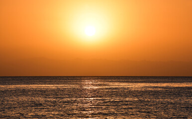 Sunrise over the sea. The bright yellow-gold color of the sky. The glare of the sun and a slight ripples on the surface of the water. A beautiful start to the day