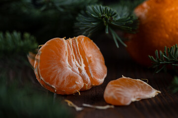 A peeled tangerine on a wooden table among spruce twigs