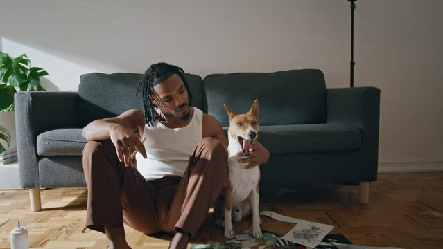 Positive man posing pet home zoom on. African american guy embracing yawning dog