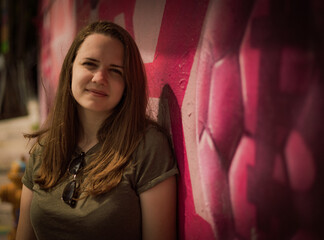 Obraz na płótnie Canvas Young and beautiful woman leans against a colorful wall and poses for the camera - typical street style - travel photography