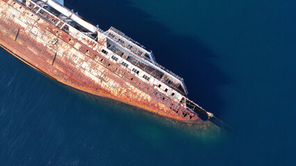 Aerial top down photo of capsized abandoned passenger ship wreck left to rust near shore