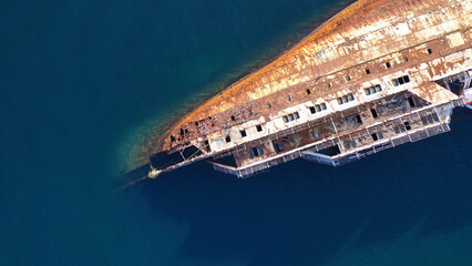 Aerial top down photo of capsized abandoned passenger ship wreck left to rust near shore