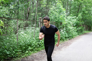 Portrait of sporty and handsome man in black sportswear walking in the eco park. Healthy lifestyle and running in open air concept