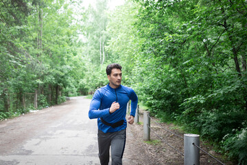 Sporty man in blue sportswear walking on the road close to the forest after jogging