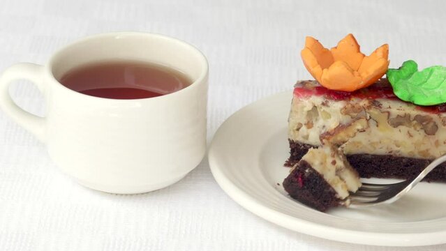 pastry piece slice of cake rectangle shape on white plate and black tea in cup.strawberry cake walnuts orange flower green leaf or pink macaron decoration.fork cutting the desert.tasty morning delight