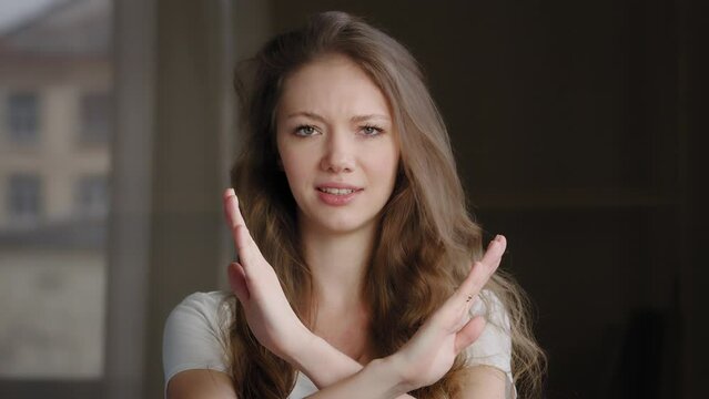 Close-up female portrait young caucasian woman showing prohibition sign crossing arms making refusal gesture negative shaking head dissatisfied serious girl says no refuses demonstrates stop gesture