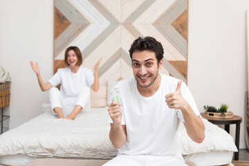 Happy man sitting on the bed, holding tablets and demonstrating his happiness after solving his erectile dysfunction problem