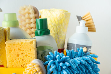 Brushes, bottles with cleaning liquids, sponges, rag and yellow rubber gloves on white background. Cleaning supplies in the yellow bucket on the wooden floor. Cleaning company service advertisement - obrazy, fototapety, plakaty