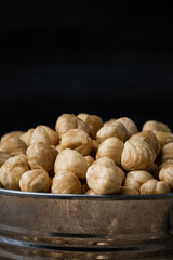 A pile of peeled hazelnuts in a metal bowl on the black background. Healthy nutrition concept. Traditional rustic agricultural background. Copy space for a free text. Macro shot