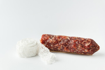 Sausage casing and cotton string roll for butchers. Elastic netting for roasting, boiling or smoking cold meat. Salami sausage on the white background.