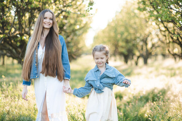 Naklejka na ściany i meble Young beautiful mother hold kid girl daughter wear similar denim jackets and white dresses in meadow outdoor. Motherhood. Family lifestyle.