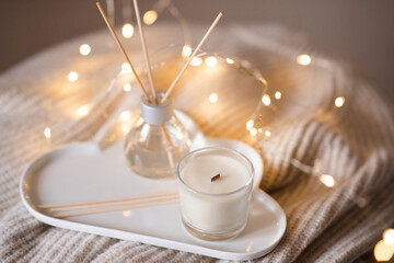 Home liquid perfume in glass bottle with bamboo sticks and scented candle on tray at coffee table...