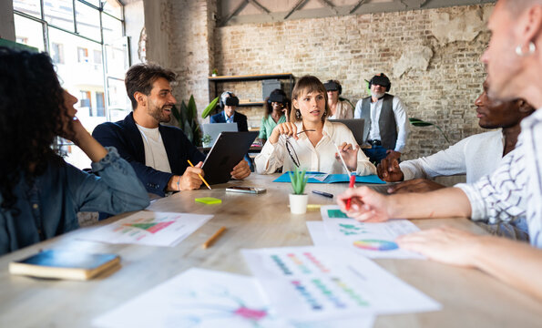 Young group of creatives discusses about new digital projects and digital marketing. At the back of the room a group of colleagues interact in the metaverse while wearing vr glasses