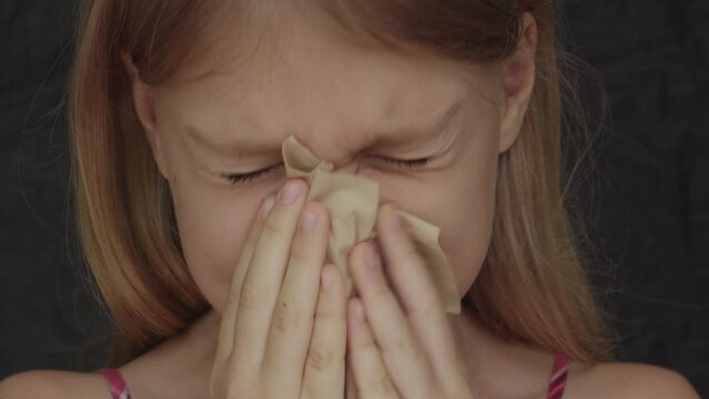 Close-up of a caucasian teen girl blowing her nose on a napkin indoor.