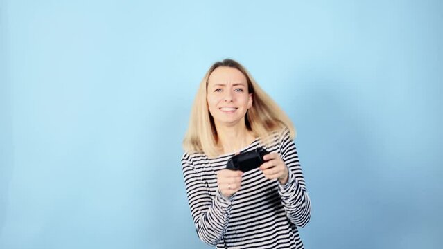 Excited cute young woman with joystick controller playing video games on blue background alone Happy blond female have fun relax after hard work day isolated Game addiction concept