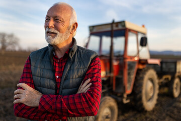 Senior farmer in front of tractor in field