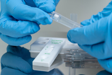 Person in blue gloves performs COVID-19 rapid test at home using personal home test kit for in...