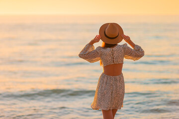 Young beautiful woman at straw hat on the beach at sunset