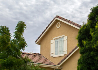 Suburban House gable window on stucco wall with cloudy sky background, Menifee, California
