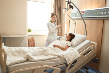 Obraz premium Medical worker stands at bedside of patient and checks dropper