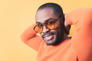 Close up of a portrait of a dark-skinned man smiling in orange sunglasses while posing with his...