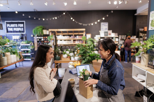 Happy, Friendly Business Owner Helping Customer Buying Plant In Shop