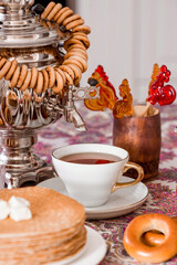 Russian traditions. Russian holiday Maslenitsa. Still life with a cup of tea, a stack of pancakes, sour cream, honey, cubes of butter, bagels, dried fruits, caramel cockerel and samovars.