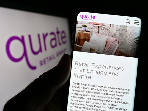 Stuttgart, Germany - 01-01-2023: Person holding cellphone with webpage of US media company Qurate Retail Inc. on screen in front of logo. Focus on center of phone display.