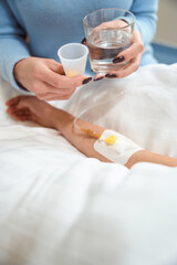 Adult woman gives pills and glass of water to sick child