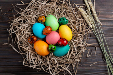 Painted multicolored eggs in a nest made of paper on a wooden background