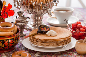 Russian traditions. Russian holiday Maslenitsa. Still life with a cup of tea, a stack of pancakes, sour cream, honey, cubes of butter, bagels, dried fruits, caramel cockerel and samovars.