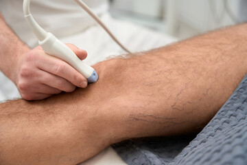 Professional orthopaedist running an ultrasound check on human knee