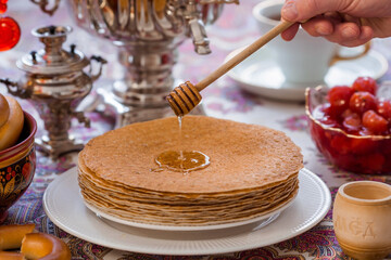Russian traditions. Russian holiday Maslenitsa. Still life with a cup of tea, a stack of pancakes, sour cream, honey, cubes of butter, bagels, dried fruits, caramel cockerel and samovars.