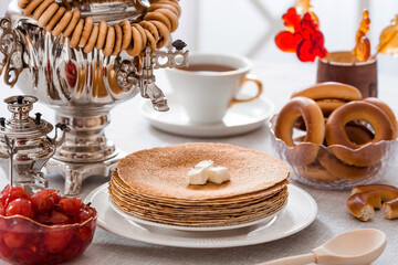 Russian traditions. Russian holiday Maslenitsa. Still life with a cup of tea, a stack of pancakes, sour cream, honey, cubes of butter, bagels, dried fruits, caramel cockerel and samovars.