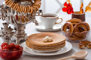 Russian traditions. Russian holiday Maslenitsa. Still life with a cup of tea, a stack of pancakes, sour cream, honey, cubes of butter, bagels, dried fruits, caramel cockerel and samovars.