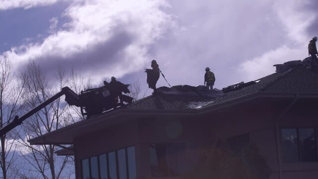 Roofers on a roof carrying shingles with clouds in the background 4K