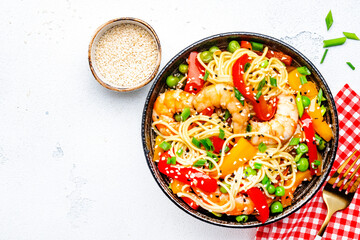 Stir fry noodles with shrimps, red and yellow paprika, green pea, chives and sesame seeds in ceramic bowl. Asian cuisine dish. White stone kitchen table background, top view