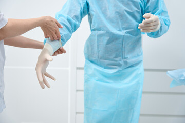 Close up of doctor in light-blue disposable medical suit putting gloves on