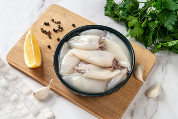 Fresh squid tubes in a bowl. Small calamary fillet and parsley prepared for cooking. Raw squid...