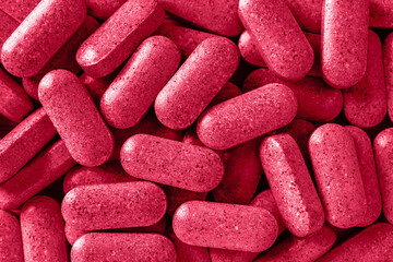 Multivitamin everyday pills toned viva magenta color. Heap of daily herbal tablets close-up texture. Medical dietary supplements and herbal medicine. Color of the year 2023.