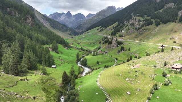 Aerial of swiss mountain rage and meadow field. Small river runniing through green landscape. Beautifull alps aerial and high peas of mountain range in the background.