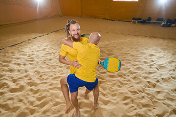 Man are jumping on partner while playing beach tennis